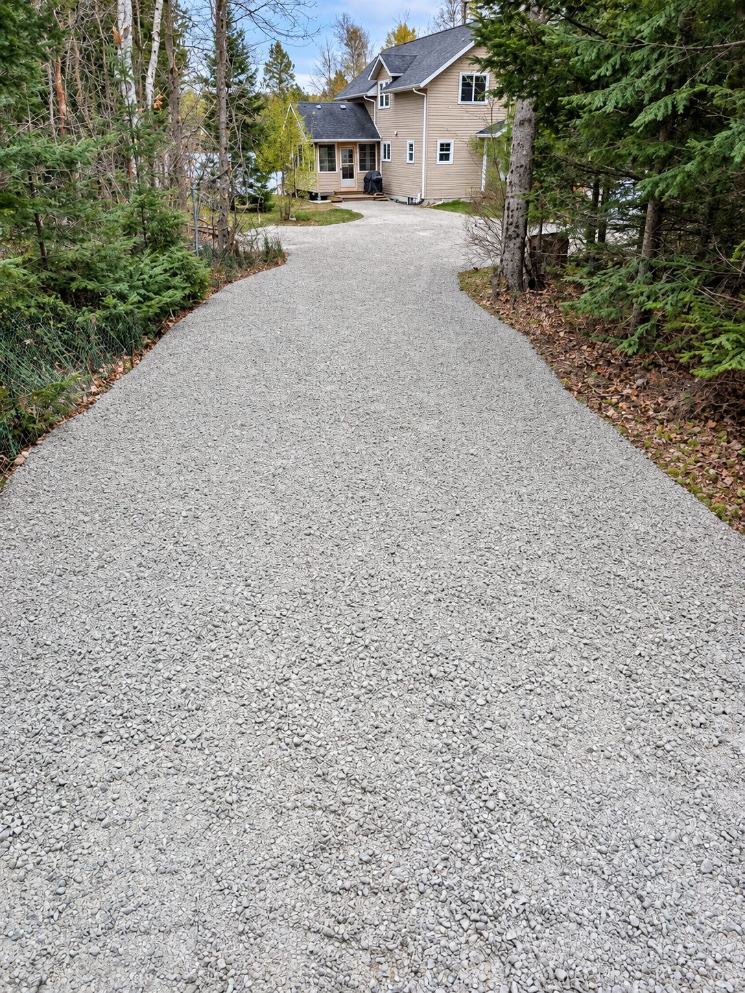 Fresh gravel driveway leading to a home surrounded by woods
